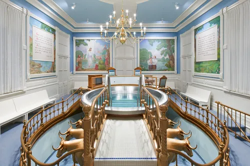 Interior image of the Manti Utah Temple. The image features the Baptistry. We see the font and the oxen below. There is art of the Savior painted on the walls around the font.
