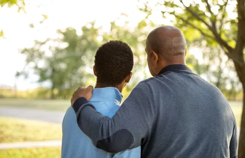 a father places his hand on his son’s shoulder as they look into the distance