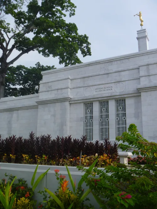 The side of the Villahermosa Mexico Temple, with a view of windows, the spire with the angel Moroni, and some flowers on the grounds.