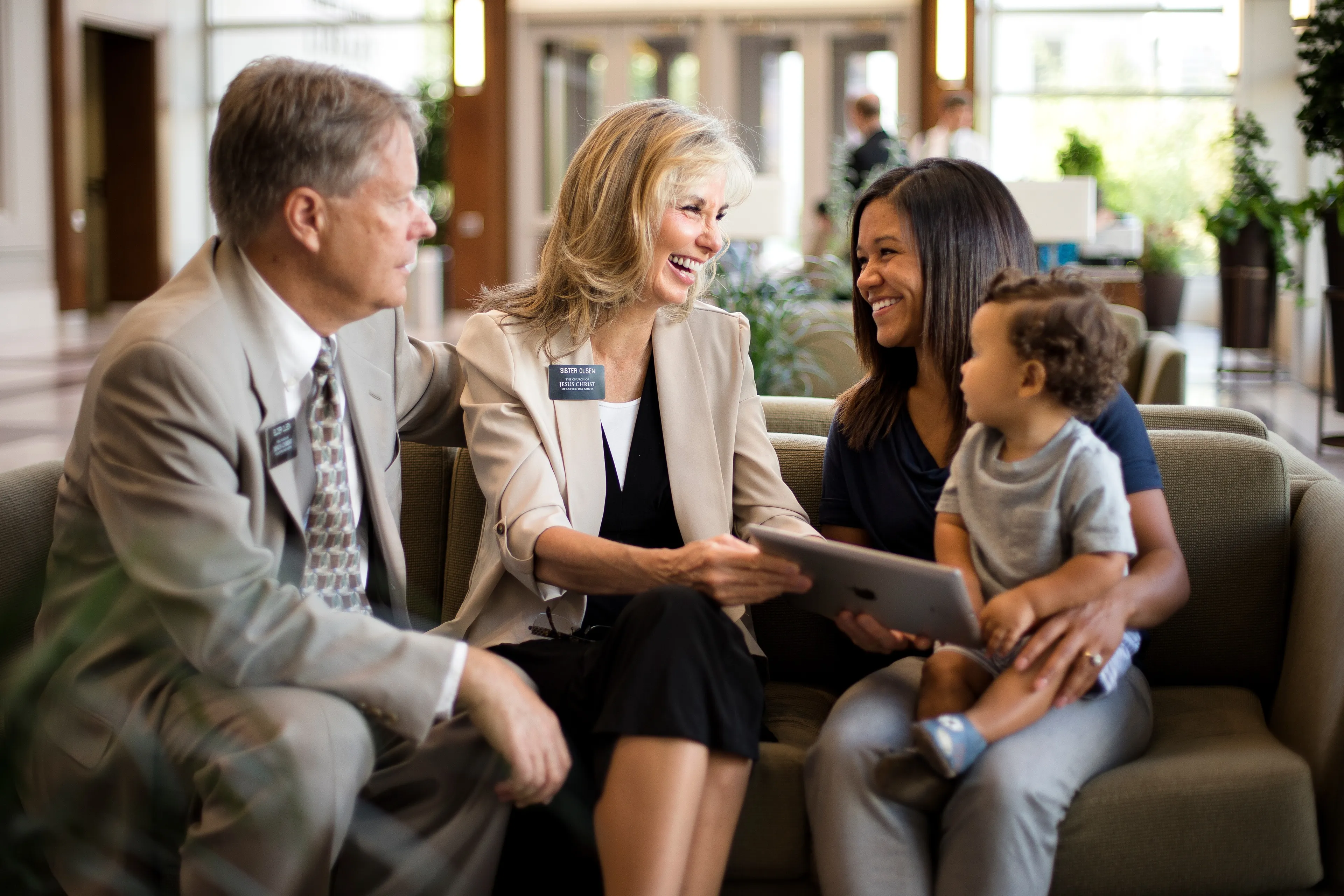 A senior missionary couple using an iPad to teach a woman who is holding a baby.  