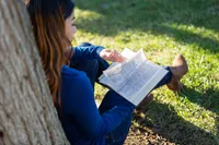 A woman studies the Bible while sitting down under the shade of a tree