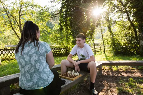 A young man sits outside and plays chess with a young woman