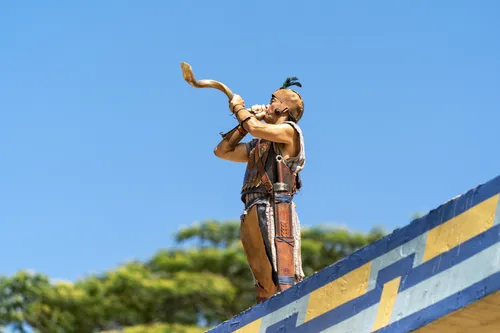 A man stands near the tower and blows a horn to call the people to hear King Benjamin in the Land of Zarahemla.