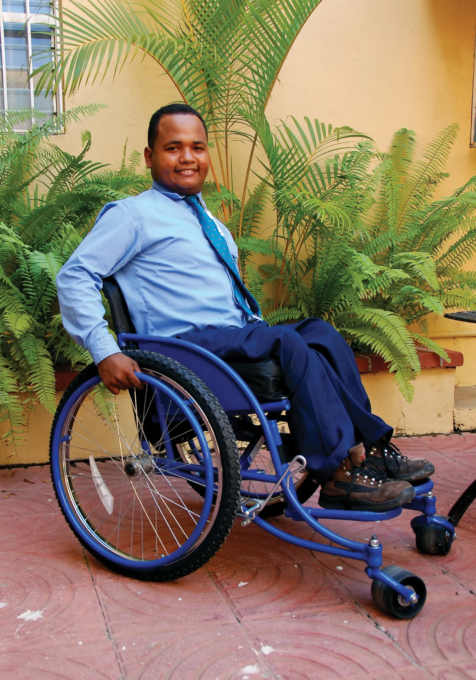 A man from the Dominican Republic sitting outside in a new blue wheelchair.