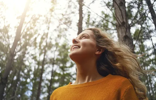 blonde young woman looking up in the forest