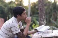 A young man holding scriptures and pondering.