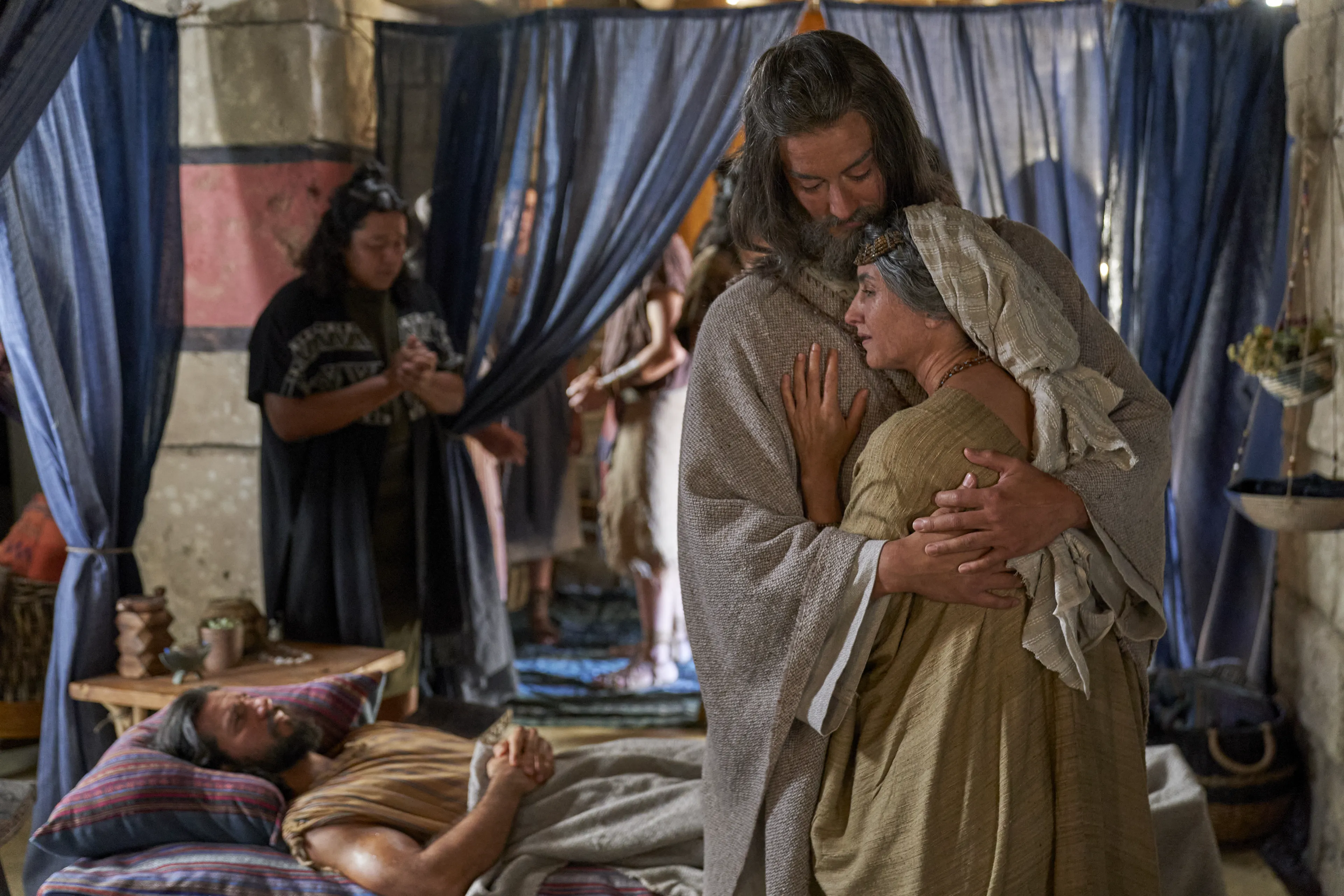 Alma the Elder holds his wife as Alma the Younger lays in bed, struck dumb.