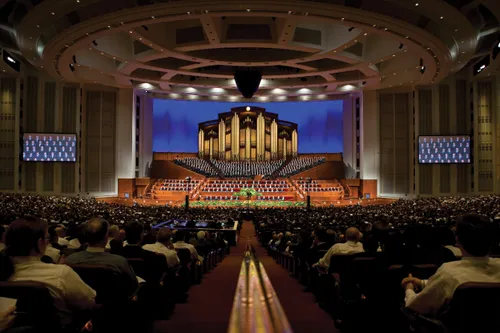The congregation on both sides of the long aisle leading to the stand, where the General Authorities and the choir are sitting.