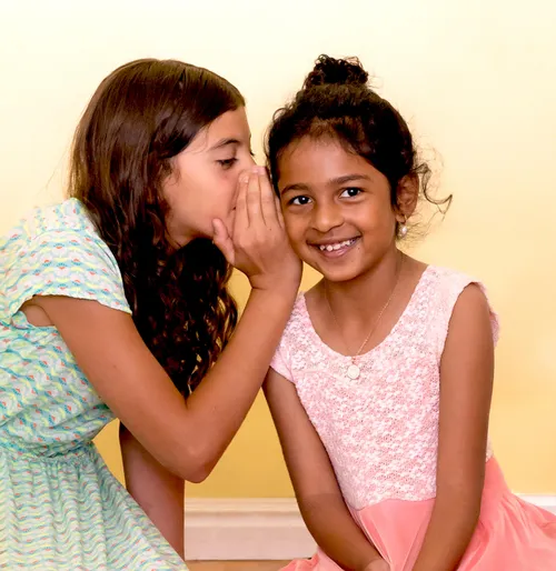 girl whispering in another girl’s ear