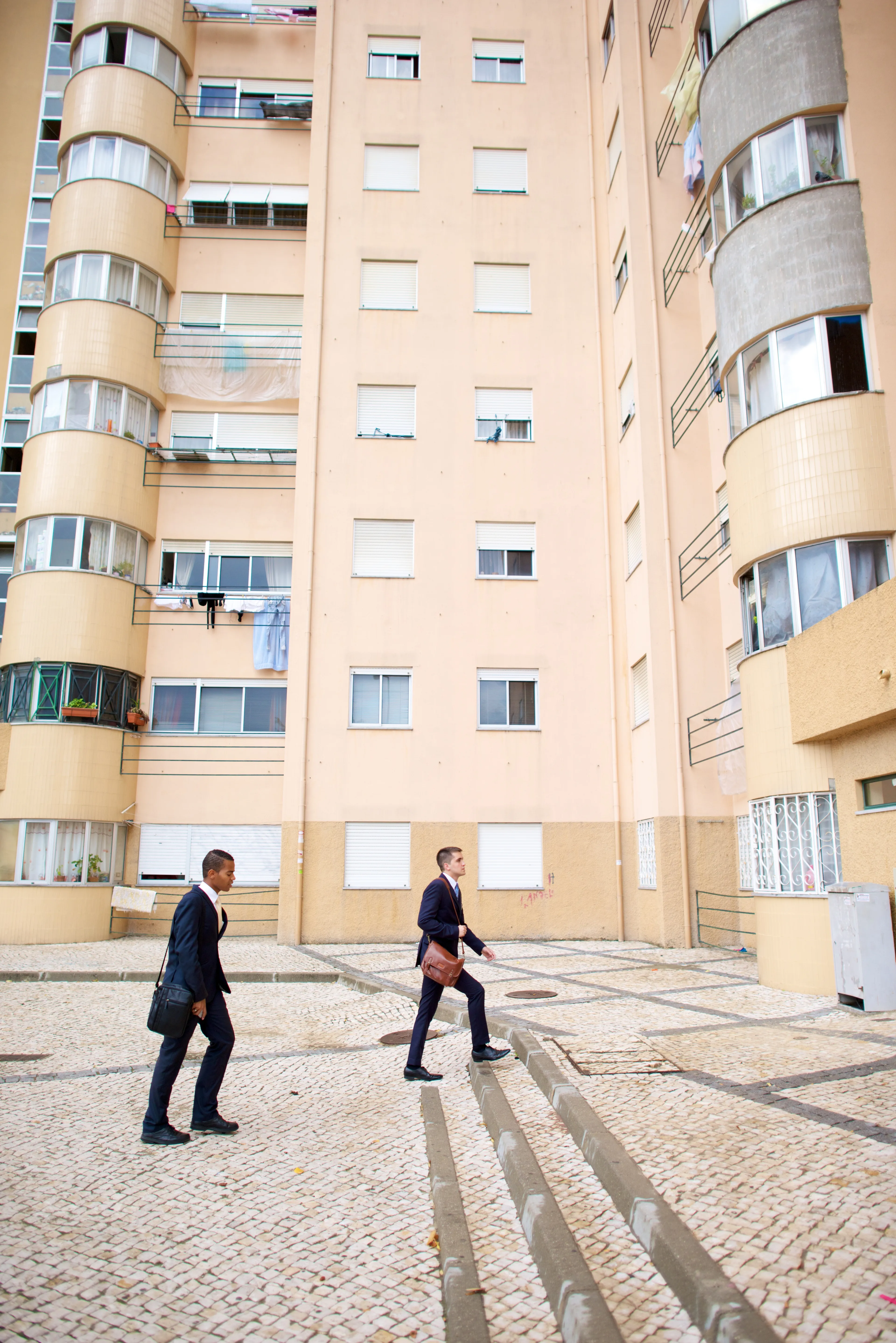 Two elder missionaries walking beside tall buildings in Portugal.