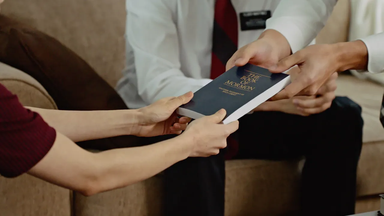 Two elder missionaries hand a copy of the Book of Mormon to a woman