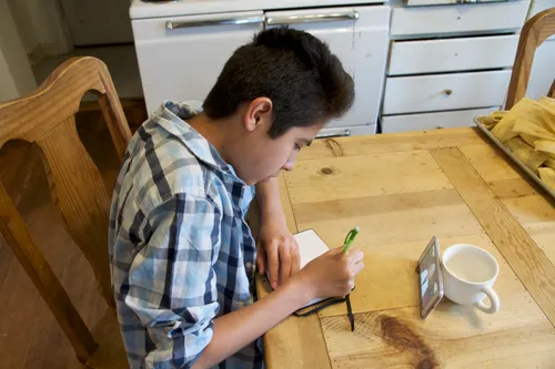 young man taking notes while watching general conference on a phone