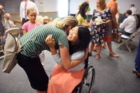 A girl in a wheel chair hugs a friend as they greet each other after a church meeting