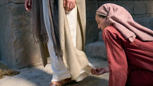 a woman with an issue of blood reaches out to touch the hem of Jesus Christ’s garments
