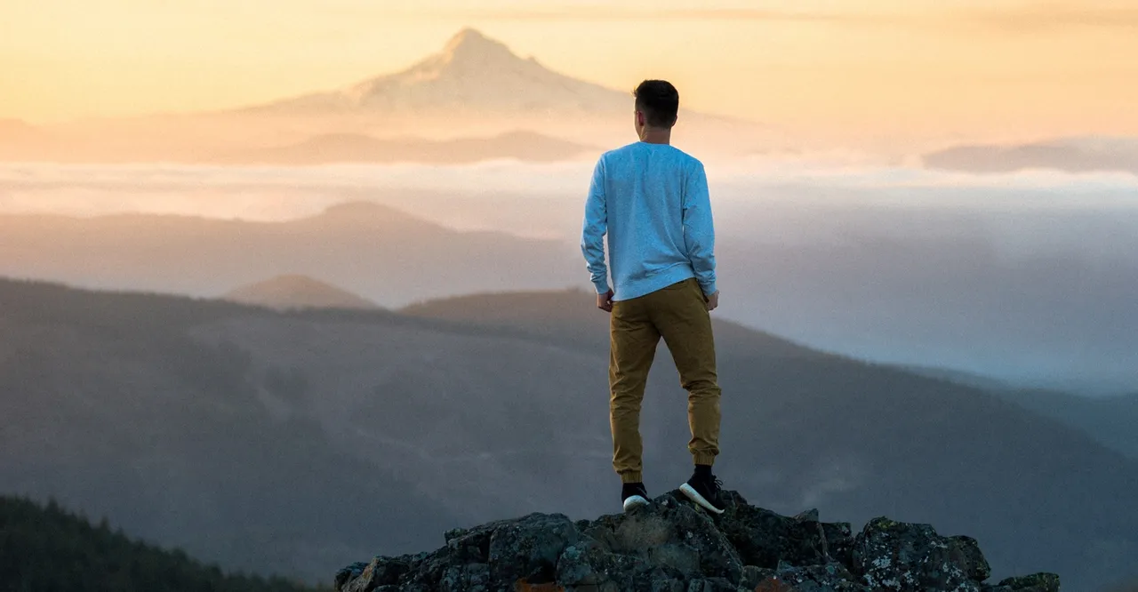 A young man stands on a mountain enjoying and contemplating the blessings of Jesus Christ