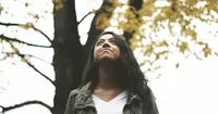 A woman is standing under a tree looking up.