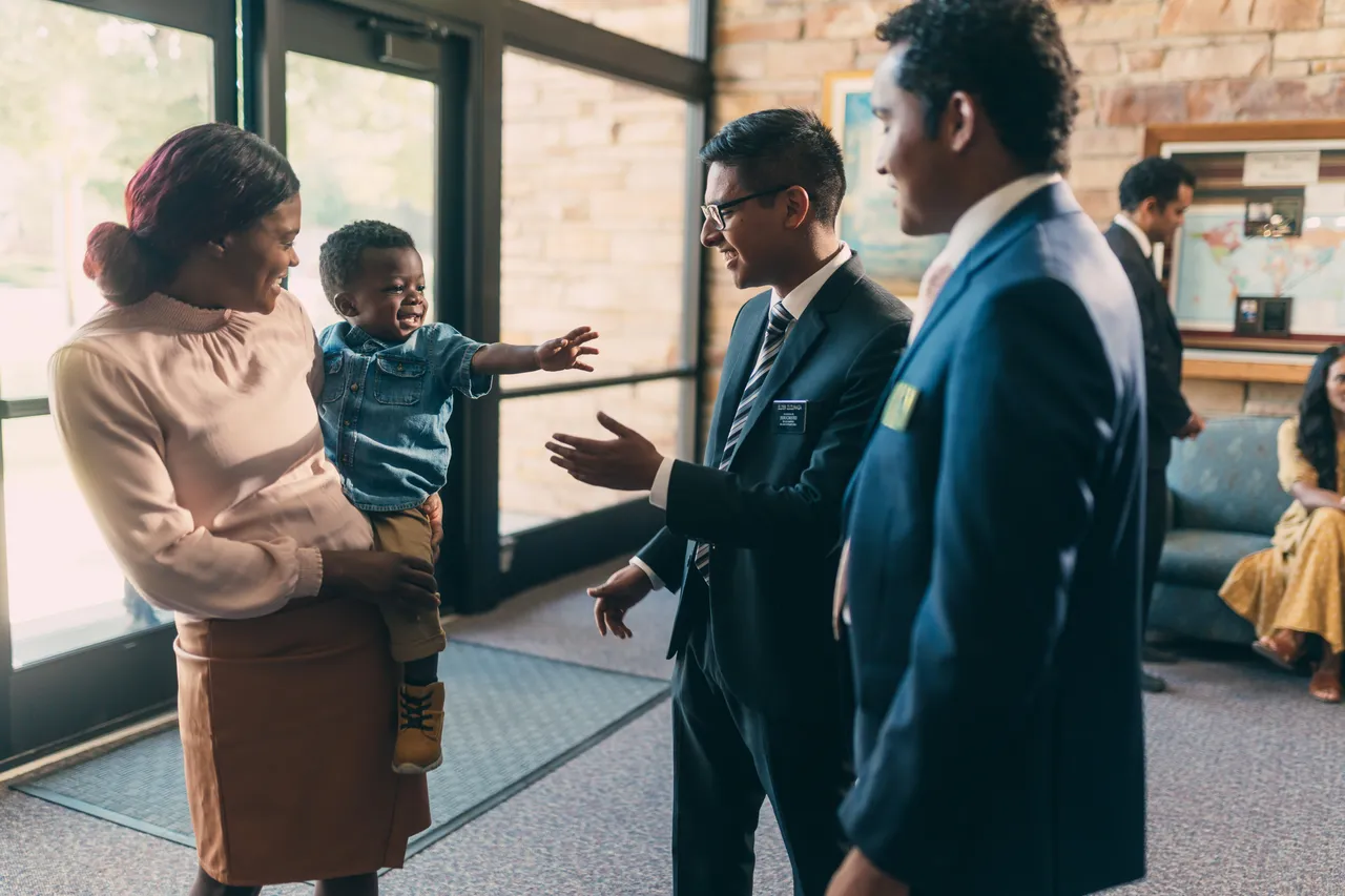 Missionaries greet a woman at the door of the church to sit with her