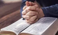 Hands interlocked rest on an open Bible