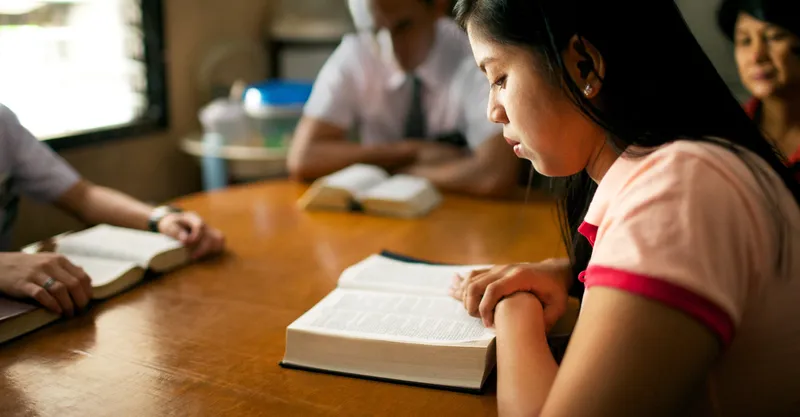 A woman sits at her kitchen table as she is taught by the missionaries the Beatitudes