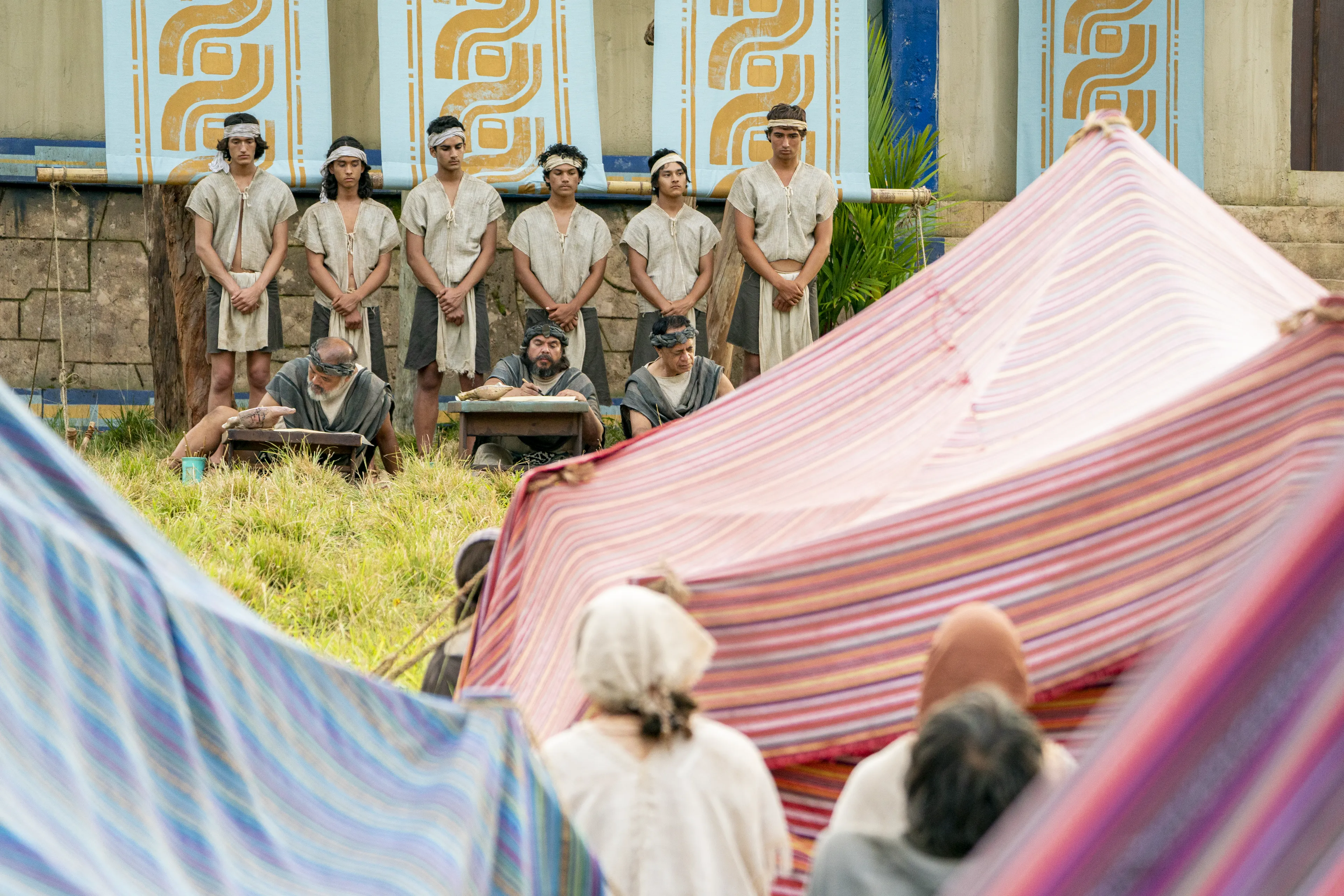 Scribes sit, taking notes on parchment of what King Benjamin is teaching in the Land of Zarahemla. Behind them, runners stand ready to take the teachings to the Nephite people.