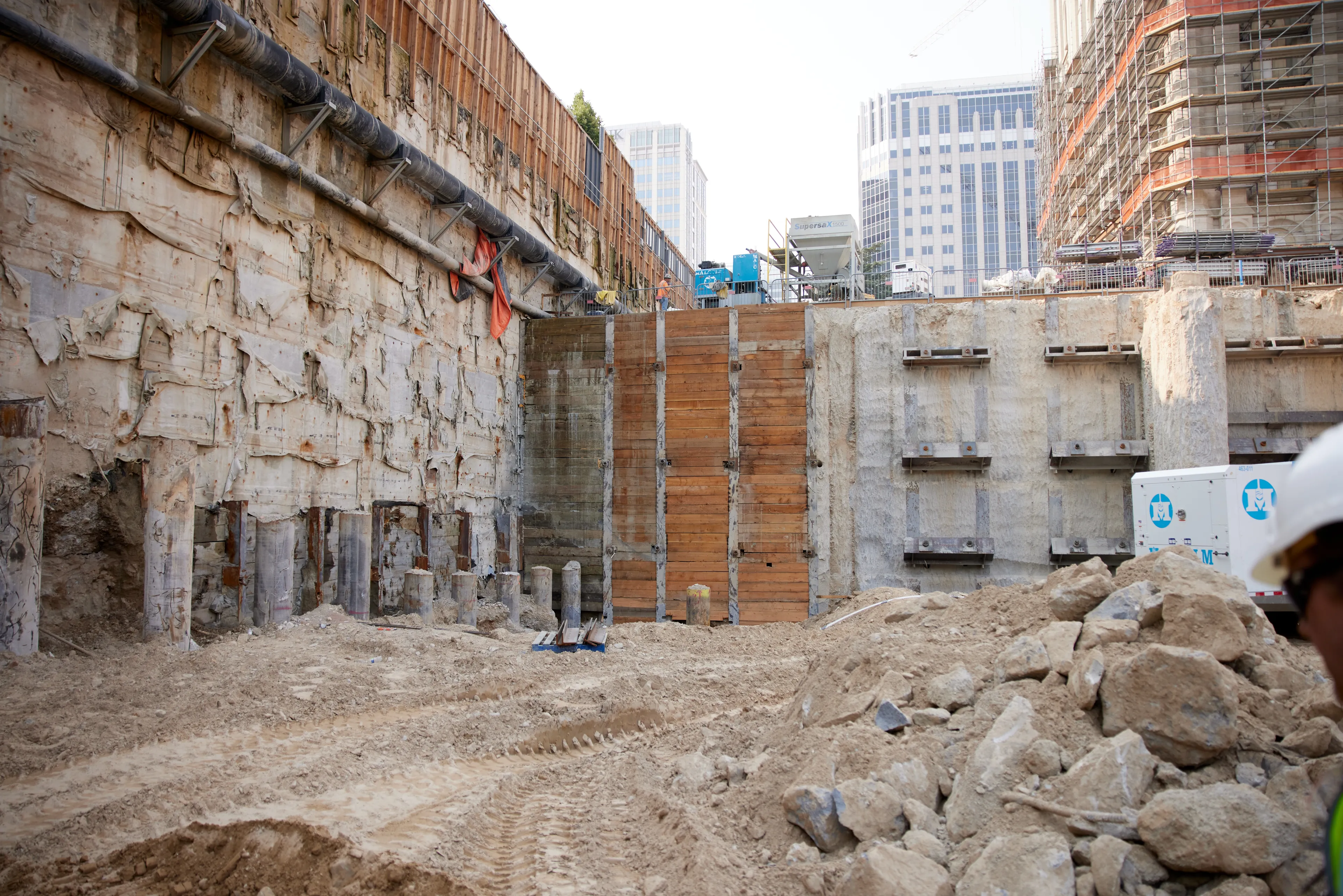 This retaining wall is made up of rows of interlocking concrete and steel columns with buttresses, each 85 feet deep. The wall shores up the soil and temple so that the excavation of the three-level underground north addition can proceed. Beams attached to the wall, called walers, help keep the soil in place by fastening long tension cables deep into the earth with grout. The photo was taken in August 2021.