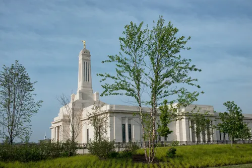 A side view of the Indianapolis Indiana Temple, including grass, trees, and a fence.