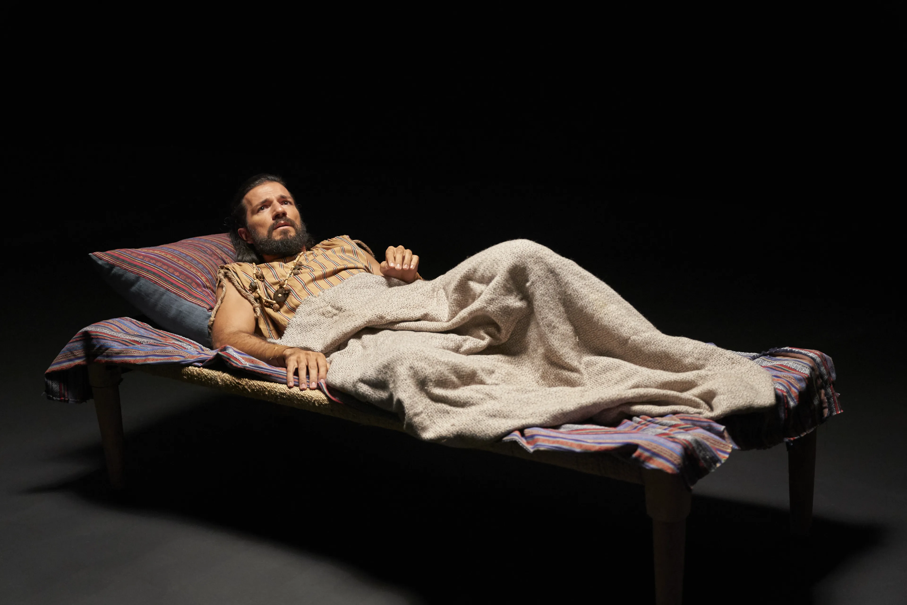 Alma the Younger lies on his bed, alone in a desolate space.