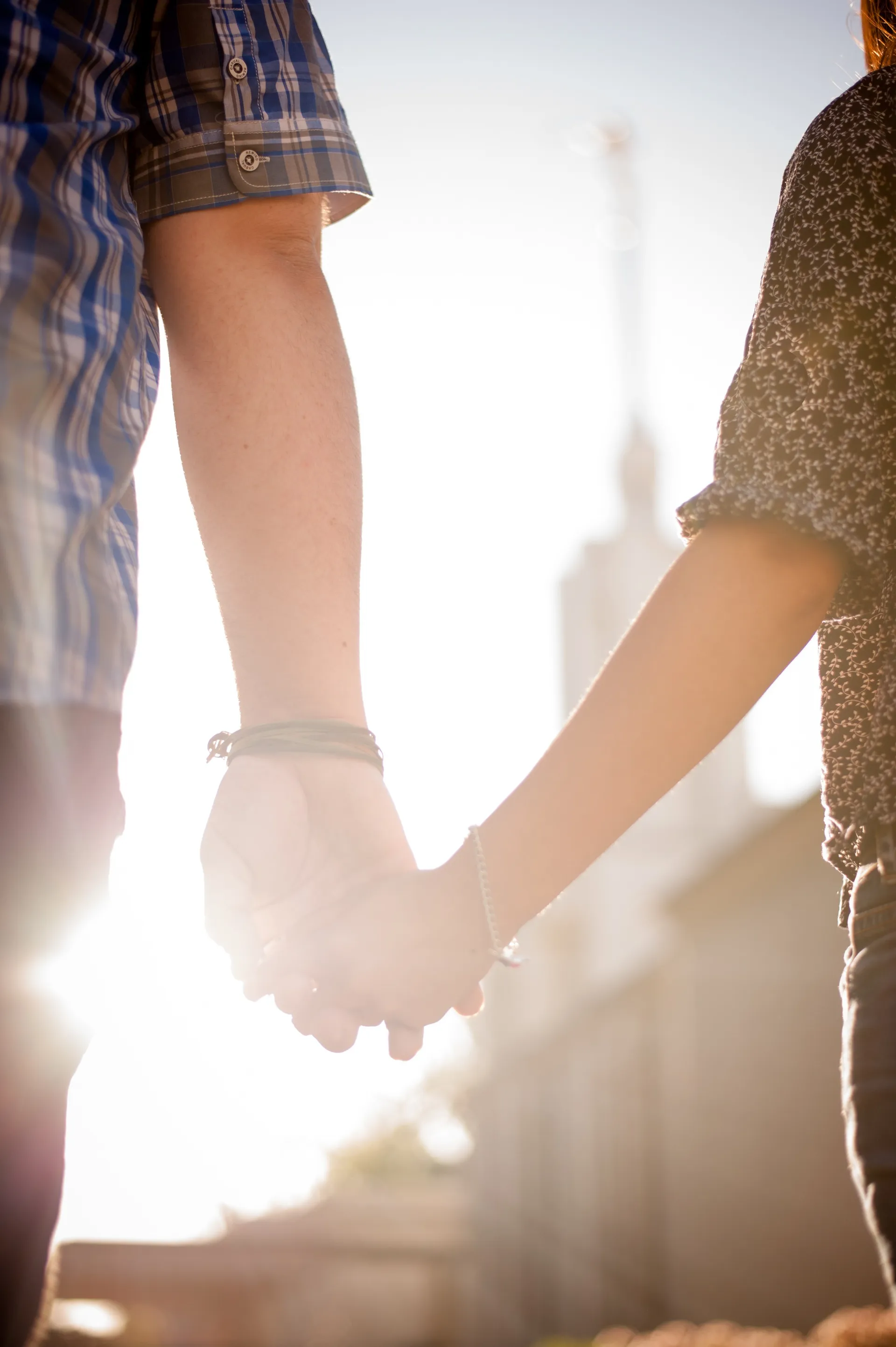 A close-up view of a couple holding hands, with a temple in the distance.
