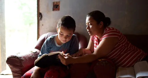 wanita membantu kanak membaca tulisan suci