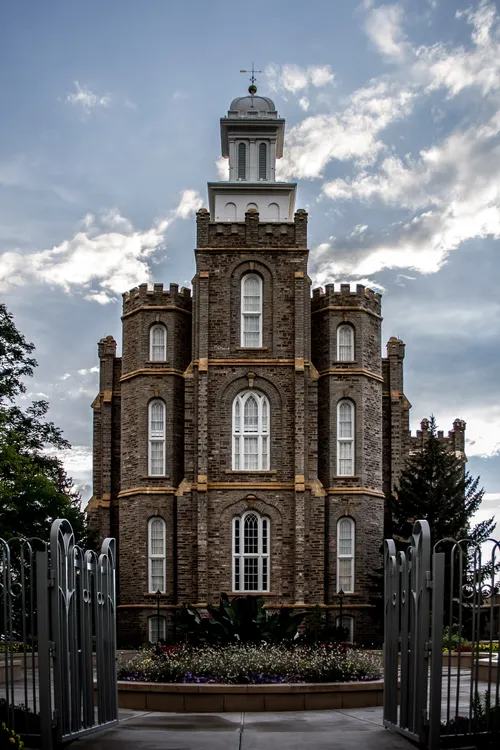 The Logan Utah Temple, with the temple’s silver gate open on the path leading up to a flower bed in front of the building.