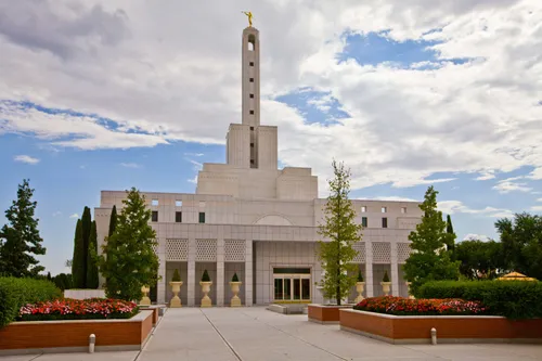 The Madrid Spain Temple entrance and grounds, with red and pink flowers and trees on a sunny day.