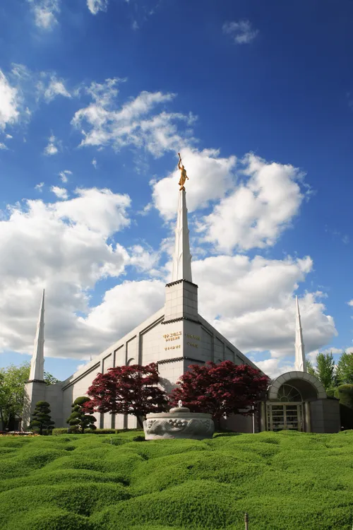 The entire Seoul Korea Temple, with a view of three spires, the entrance, the angel Moroni on top, and the surrounding grounds with trees and bushes.