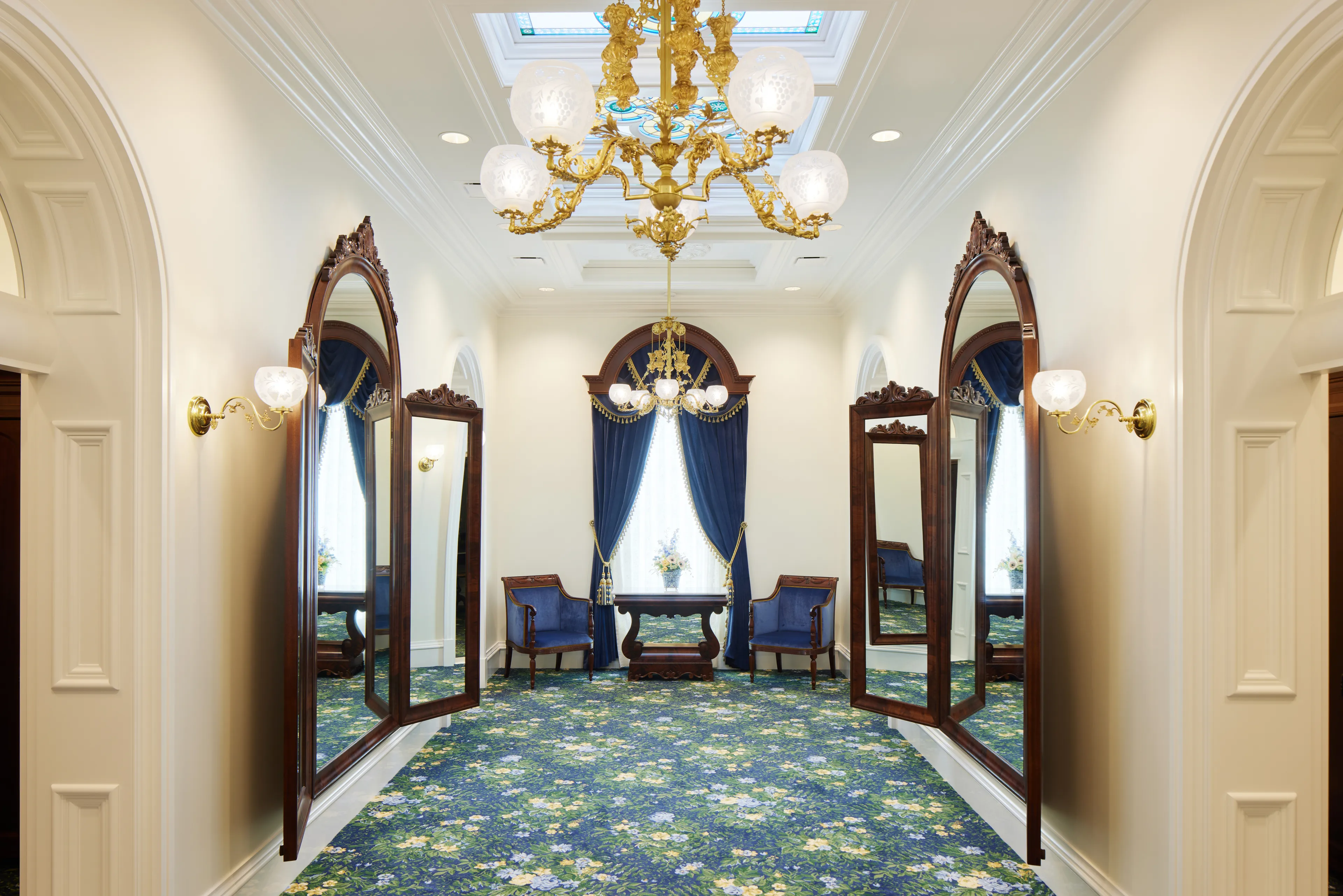 Interior image of the St. George Utah Temple. The image features the Brides’ Room. There are large windows on both sides. A chandelier hinges in the center of the ceiling. 