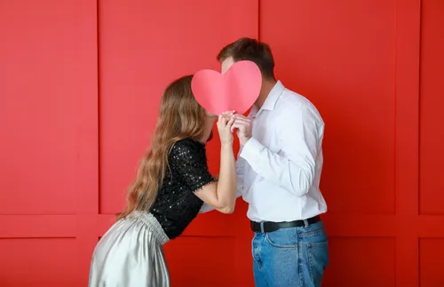 Young couple kissing behind a paper heart