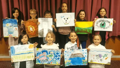 Primary children holding up paintings of God’s creations