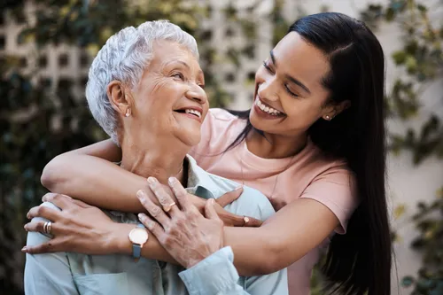 Senior Hispanic woman and her daughter smile and hug in a garden.