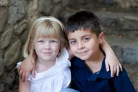A little boy and a little girl smiling with their arms around each other while sitting on stone steps.