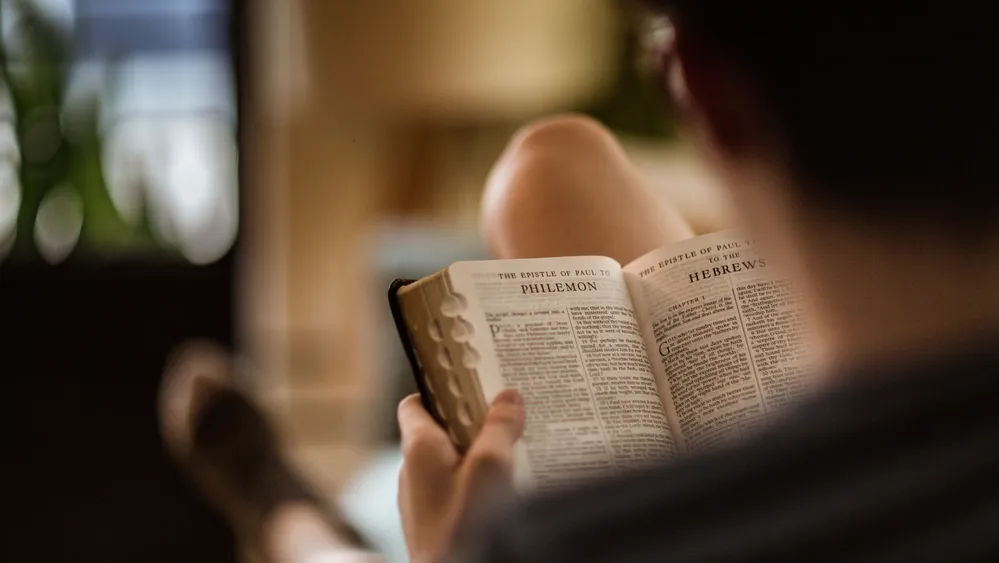Photograph of a person reading scripture. We can see the words “Philemon” from the new testament on the page. 
