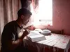 a young adult male reads the scriptures next to an open window