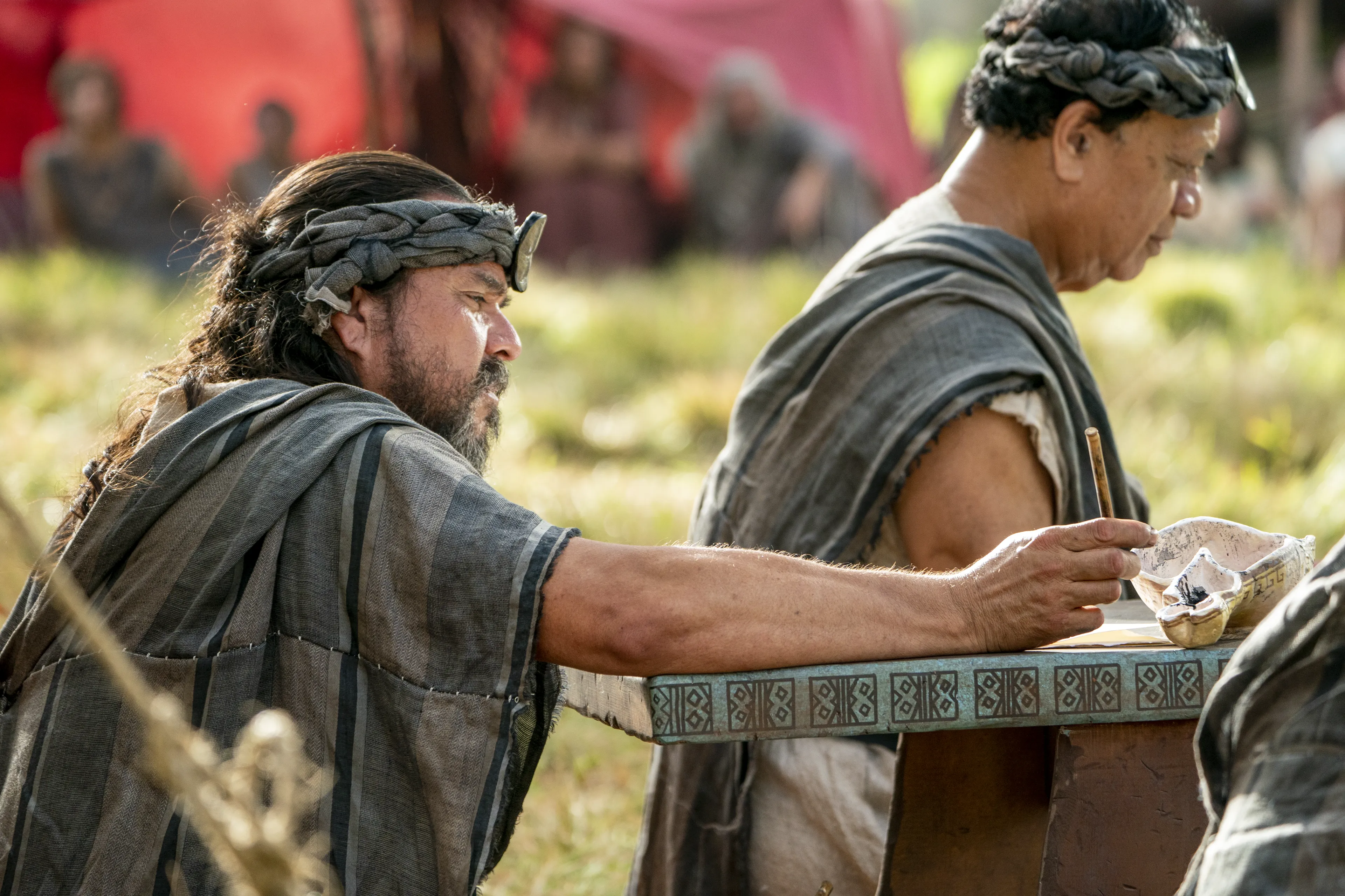 Scribes sit, taking notes on parchment of what King Benjamin is teaching in the Land of Zarahemla.