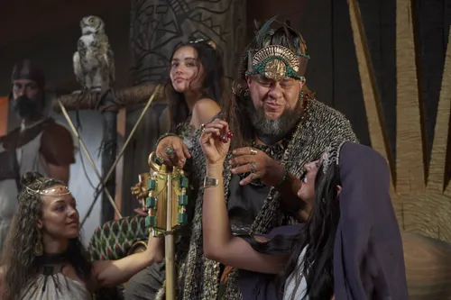 King Noah feasts with a large crowd of priests and women in his throne room.