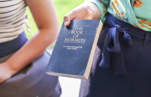 Woman holding out a Book of Mormon