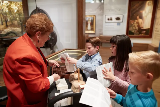 Children in the Church History Musuem. A group of children interact with the exhibits. A docent is nearby talking with them.