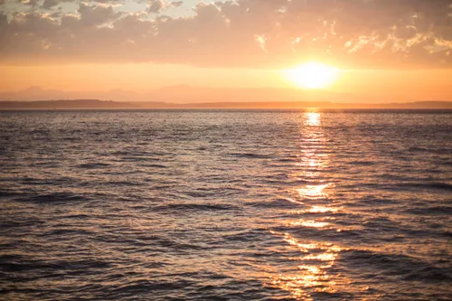The sun setting over the ocean with clouds overhead.