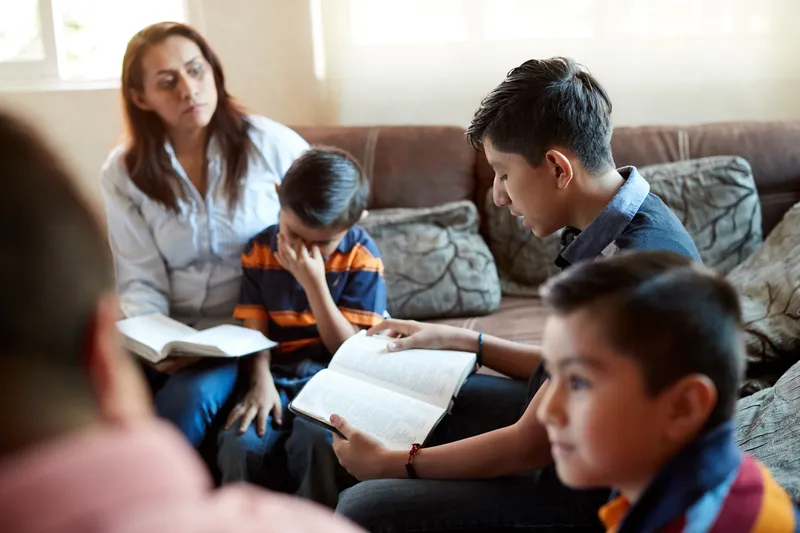 A young couple sit with their children reading and studying the scriptures