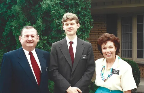 young missionary elder standing in between older couple
