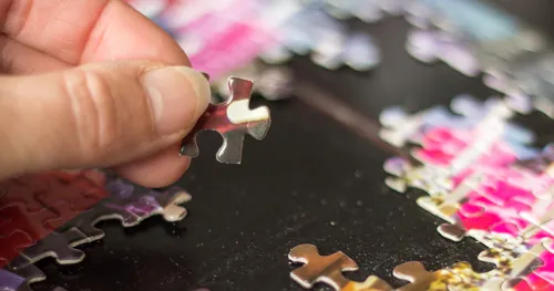 hand holding piece of jigsaw puzzle with incomplete puzzle on table