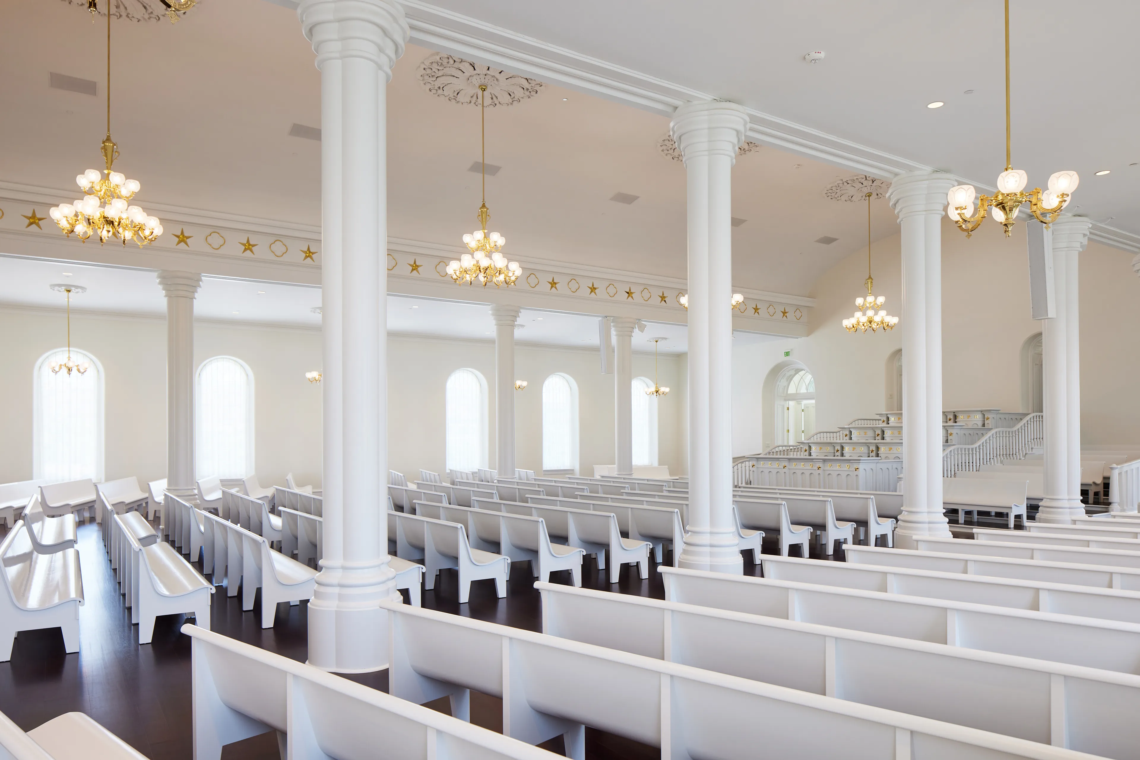 Interior image of the St. George Utah Temple. The image features the Chapel. The pews and ceiling are white with a dark wood floor. 
