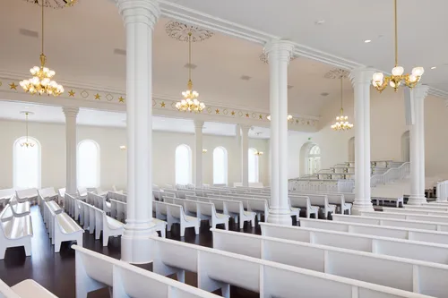 Interior image of the St. George Utah Temple. The image features the Chapel. The pews and ceiling are white with a dark wood floor. 