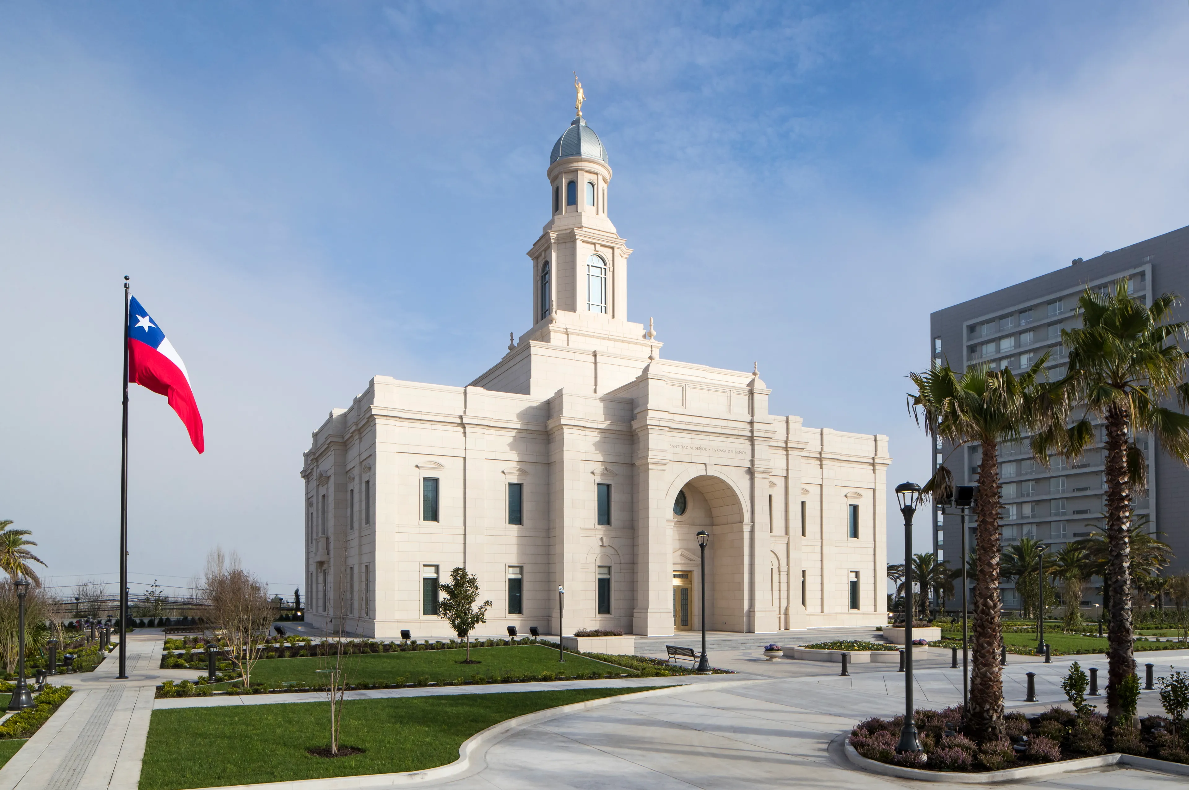 The Concepción Chile Temple on a clear day with the Chilean flag displayed on the grounds.